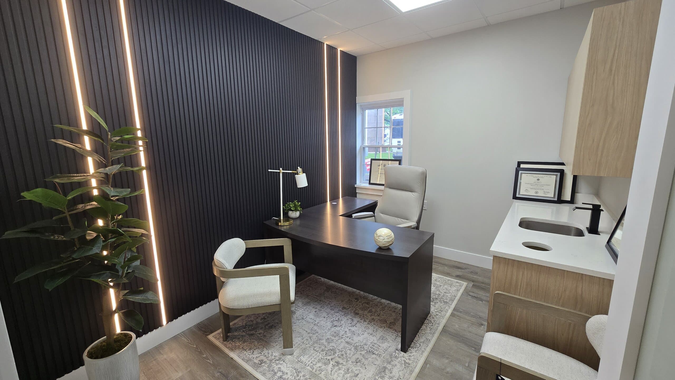 The consultation office at 360 Health Center, with a dark wood slat wall, warm accent lighting, and framed diplomas.